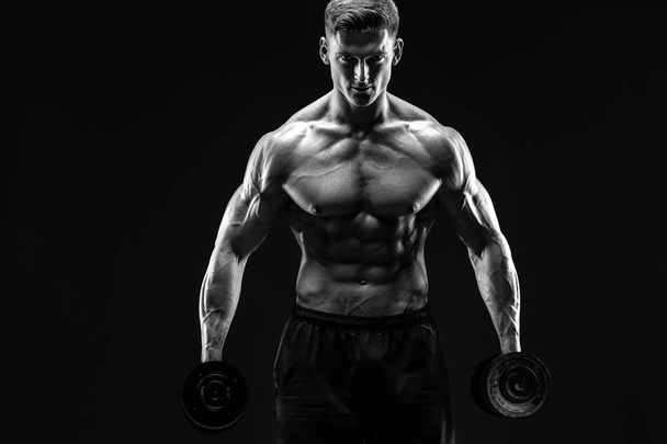 Handsome bodybuilder doing exercise with dumbbell. Studio shot. Black and white photo. - Foto, Bild