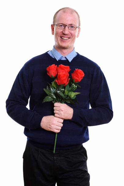 Studioaufnahme eines glücklichen Mannes, der lächelt, während er rote Rosen bereit hält - Foto, Bild