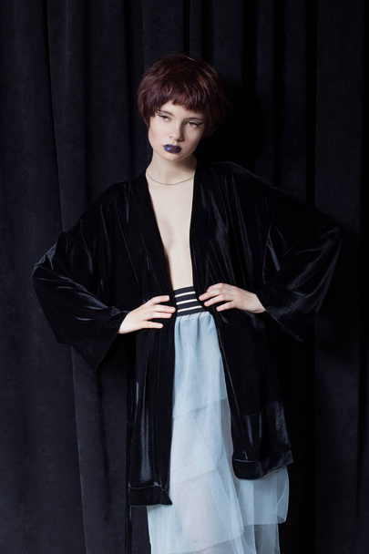 fashion shot of a beautiful young girl with a cheeky short hair style hipster in black velvet jacket in a studio on a black background - Zdjęcie, obraz