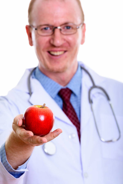 Studio shot of happy man doctor smiling while giving red apple w - Photo, Image