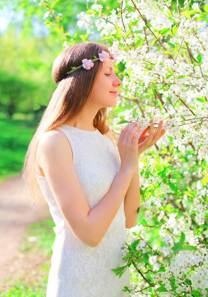Beautiful young woman with floral headband enjoys spring flowers - Foto, Imagen