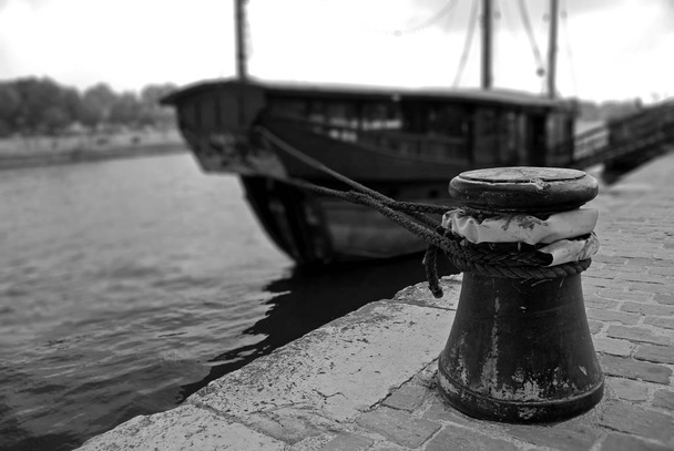 Verrostete Verankerungspoller mit Seilen am Liegeplatz. Im verschwommenen Hintergrund ankert ein Touristenboot. River Seine, Paris, Frankreich. Schwarz-Weiß-Fotografie - Foto, Bild