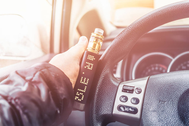 Mans hand on steering wheel of car with modern vaping device or vaporizer - Photo, Image