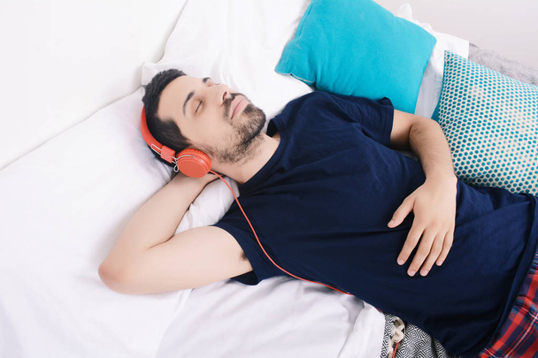 Man listening to music in bed. - 写真・画像