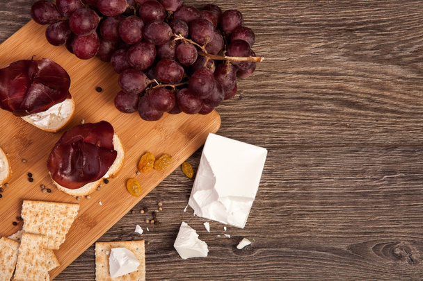 Jamón, galletas saladas, uva y queso blanco sobre fondo de madera
 - Foto, Imagen