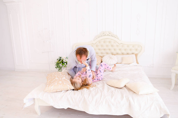 Papa kitzelt Tochter, spielt mit Mädchen im Bett zu Hause - Foto, Bild