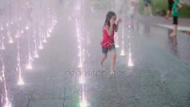 Wet little girl running through the water jets at the fountain and laughing. Child having fun in hot summer day. - Video