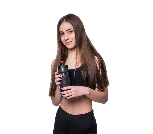 Portrait of smiling young sporty woman with a bottle of water posing in studio isolated on white background. - Photo, Image