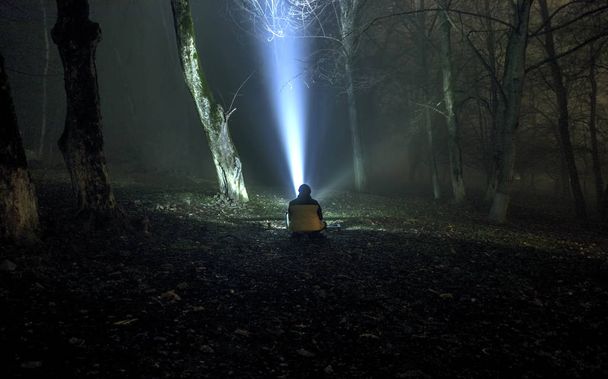 étrange silhouette dans une sombre forêt effrayante la nuit, paysage mystique lumières surréalistes avec l'homme assis sur le sol
 - Photo, image