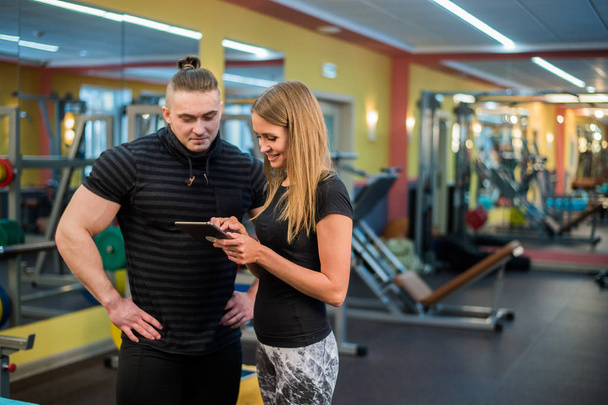 dopasowanie atrakcyjna młoda para na siłowni patrząc na tablet-pc, jak one monitorować swoje postępy i fitness - Zdjęcie, obraz