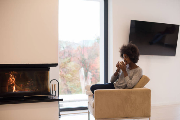black woman drinking coffee in front of fireplace - Photo, image