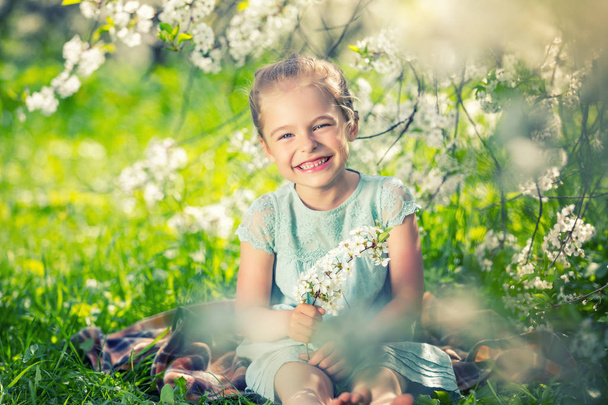 Happy little girl in cherry blossom garden - Foto, afbeelding