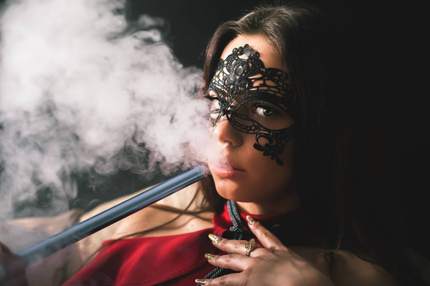 Young, beautiful girl with carnival mask smoke a hookah - 写真・画像