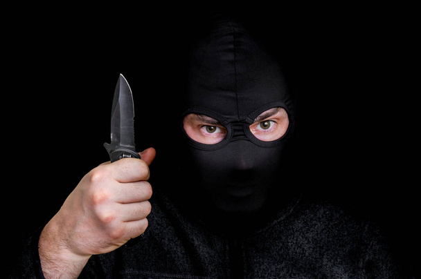 Naamioitunut mies balaclavassa veitsi eristettynä mustaan
 - Valokuva, kuva