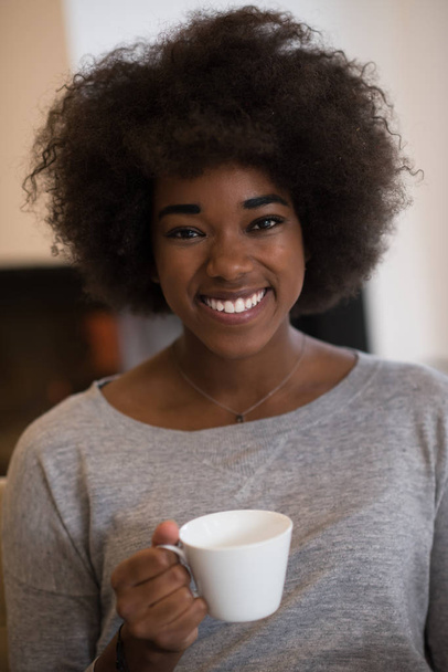 black woman drinking coffee in front of fireplace - Zdjęcie, obraz