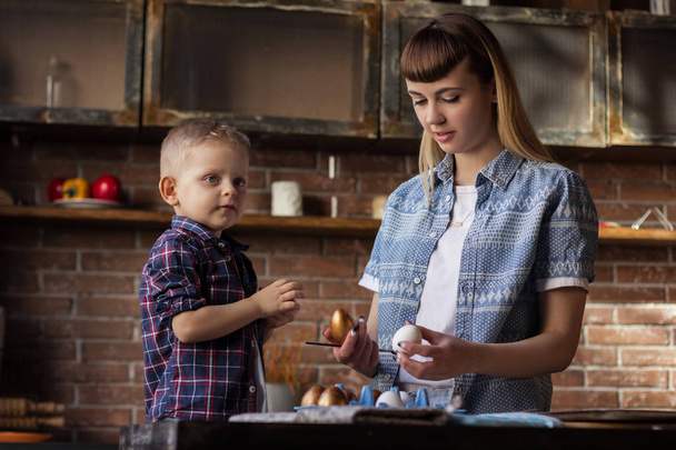 Young woman with her little brother painting Easter eggs in the kitchen - Фото, зображення