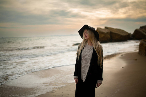 Femme en chapeau et manteau sur la plage d'hiver au coucher du soleil
. - Photo, image