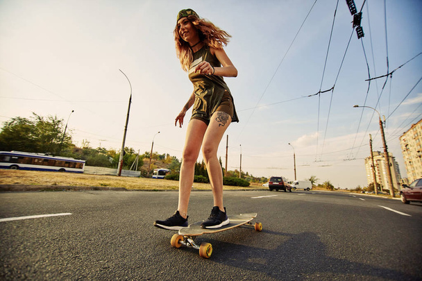 Hermosa chica joven con tatuajes montando longboard en tiempo soleado
 - Foto, Imagen