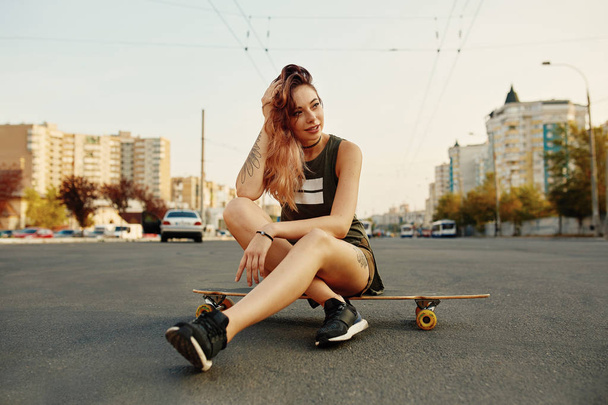 Beautiful young girl with tattoos sits on longboard - Фото, изображение