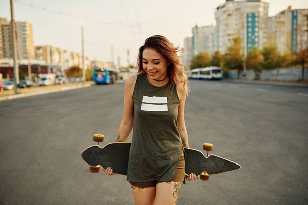 Piękna młoda dziewczyna tatuażem z longboard przy słonecznej pogodzie - Zdjęcie, obraz