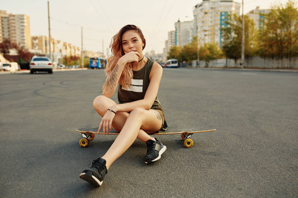 Beautiful young girl with tattoos sits on longboard - Fotoğraf, Görsel