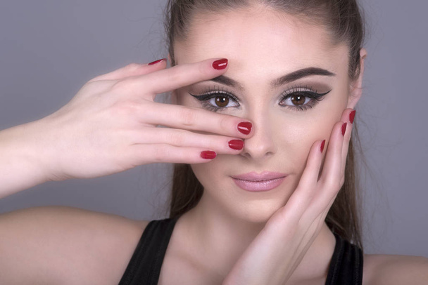 Hands and fingers with red nail polish cover a girl's face - Fotoğraf, Görsel