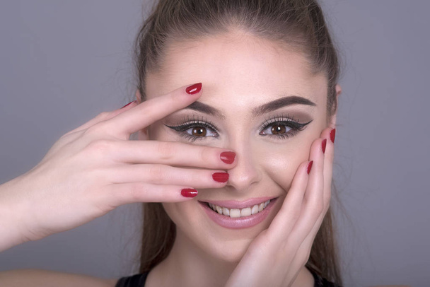 Handen en vingers met rode nagellak bedekken een girl's gezicht - Foto, afbeelding