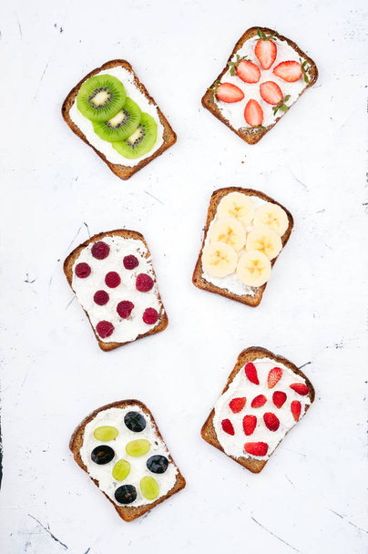 Healthy breakfast with toasts. Sweet sandwiches with cream cheese and fresh berries and fruit on white background. Healthy eating and diet concept - Photo, Image