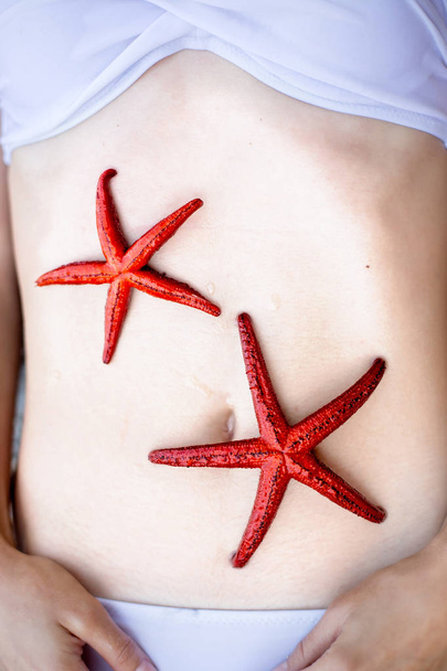 Young woman, holding red five finger starfish on the beach - Foto, afbeelding