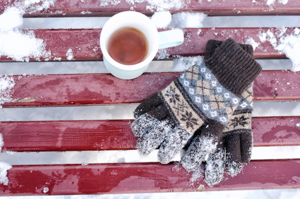 Tasse de thé et gants tricotés pour femmes sur un banc en hiver, la neige en dessous. vue de dessus
 - Photo, image