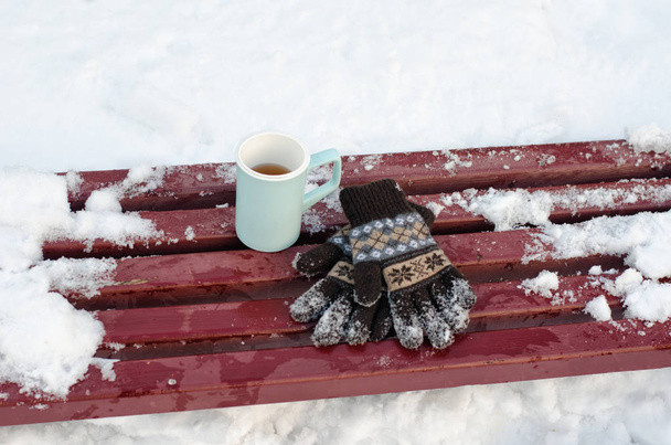 マグ茶、冬には、バック グラウンドで雪のベンチで女性のニット手袋。クローズ アップ - 写真・画像