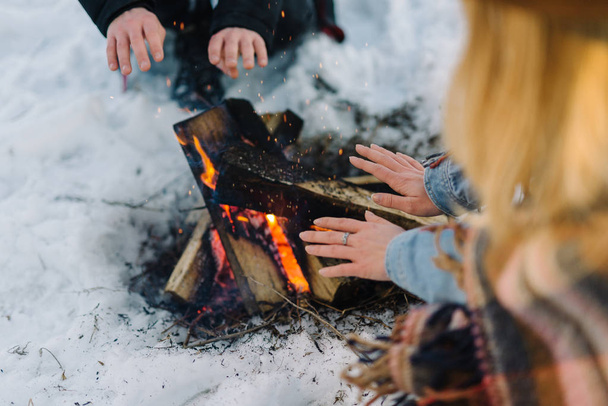 stylishly dressed young couple, sitting near the fire in the winter forest - Photo, Image