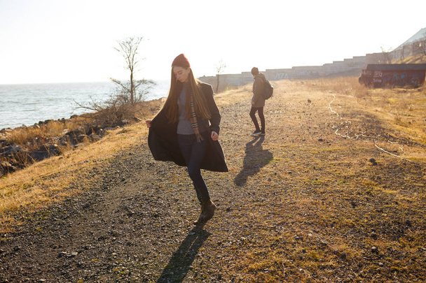 Kaunis ja tyylikäs pari kävelee kivinen ranta. Pari pukeutunut takit, hatut ja saappaat
 - Valokuva, kuva