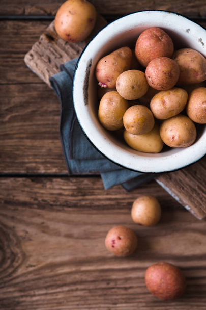 Raw potatoes in the metal bowl on the wooden table top view - Photo, image