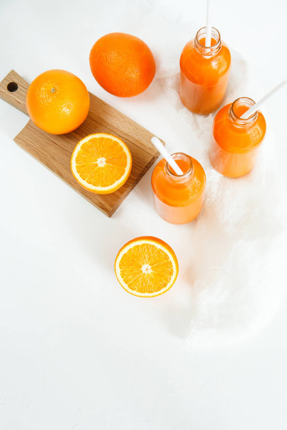 Três garrafas de suco de laranja e tubos estão sobre a mesa em um fundo branco
 - Foto, Imagem