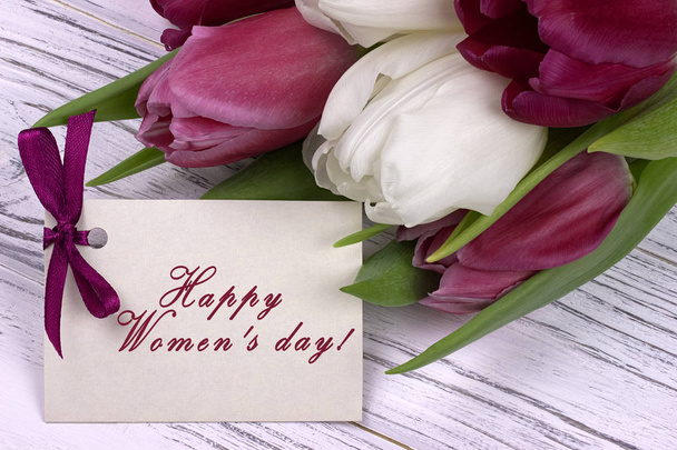 Purple and white tulips with white paper on a white wooden background and card lettering happy women's day english. Womans Day. 8 March. - Photo, Image