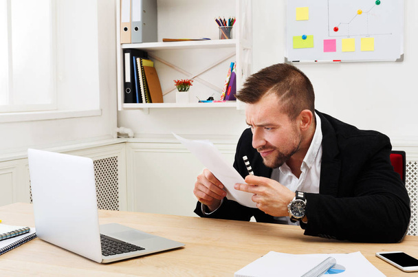 Nuori keskittynyt liikemies lukea asiakirjoja moderni valkoinen toimisto
 - Valokuva, kuva
