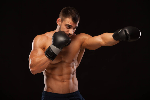 Muscular young man with perfect Torso with six pack abs, in boxing gloves is showing the different movements and strikes isolated on black background with copyspace - Zdjęcie, obraz