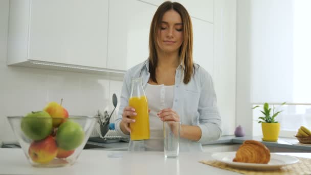 Pretty young woman in the kitchen,pouring herself a glass of orange juice. - Imágenes, Vídeo