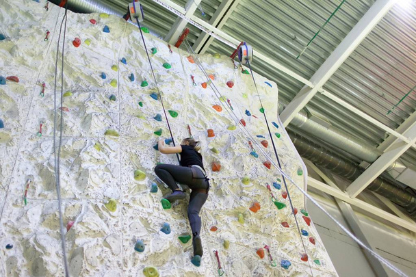 Jovem atlética praticando escalada em uma parede de rocha dentro de casa
 - Foto, Imagem