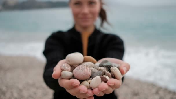 Donna tiene tra le mani un mucchio di rocce sulla riva con le onde
. - Filmati, video