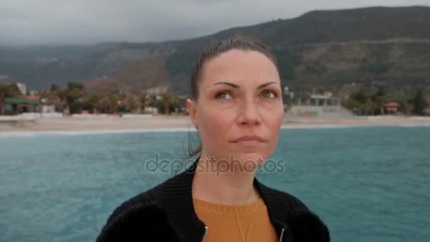 Young woman with freckles looks around the coast in cloudy weather. - Footage, Video