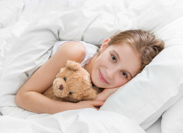Girl in bed with teddy bear, falling asleep - Fotó, kép