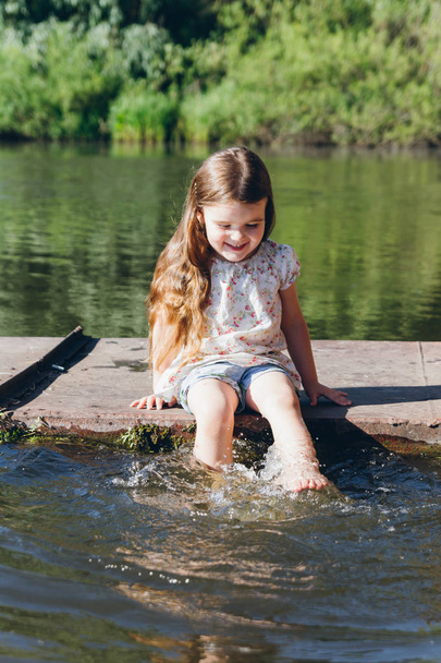 Little girl dipping feet in the water and laughing - 写真・画像