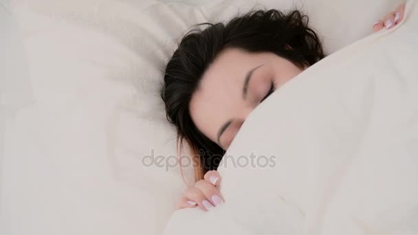 Close-up of a young beautiful woman with a funny look hiding under the blanket. Girl having fun in bed. - Séquence, vidéo