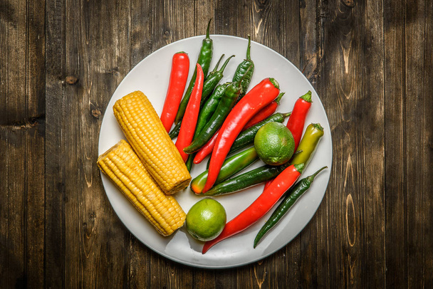Red and green chili pepper, corn on plate on wooden background - Fotoğraf, Görsel