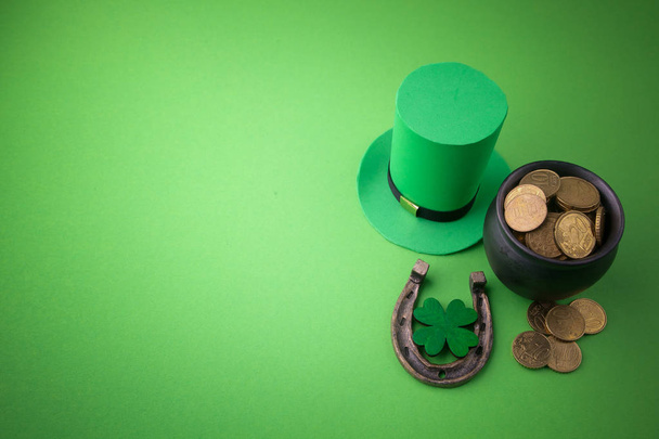 Happy St Patricks Day leprechaun hat with gold coins and lucky charms on green background. Top view. - Fotó, kép