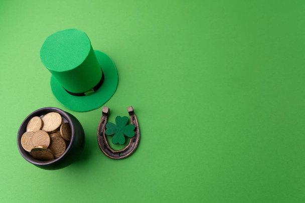 Happy St Patricks Day leprechaun hat with gold coins and lucky charms on green background. Top view. - Fotó, kép
