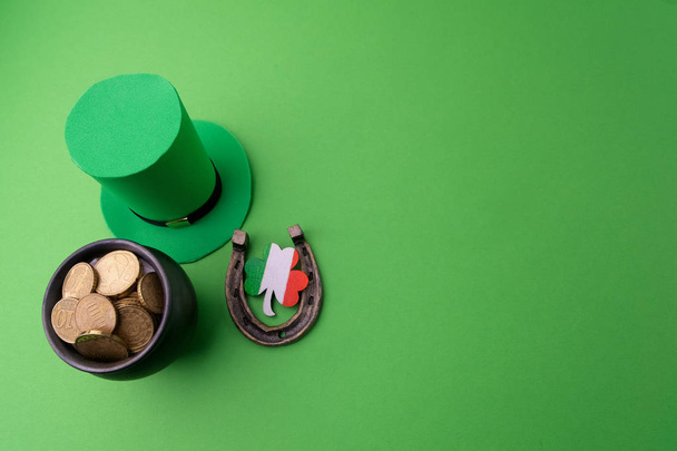 Happy St Patricks Day leprechaun hat with gold coins and lucky charms on green background. Top view. - Foto, Bild