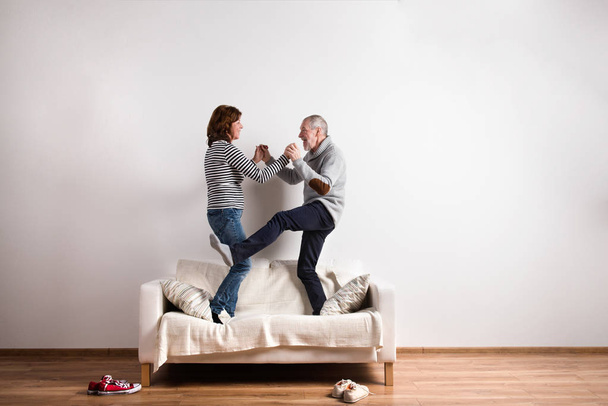 Beautiful senior couple standing on couch, dancing. Studio shot. - Fotoğraf, Görsel